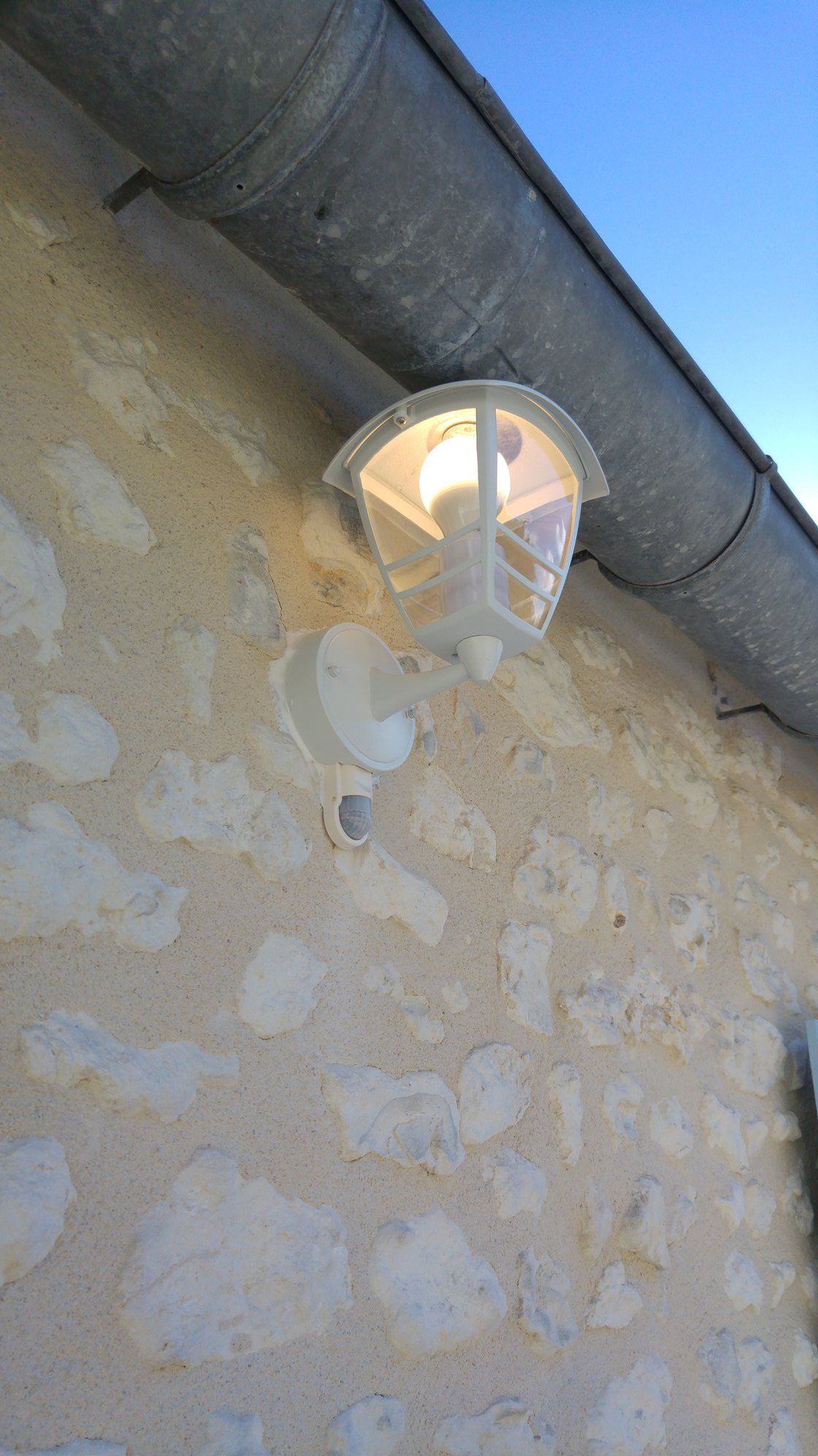 Lanterne blanche d'extérieur avec détecteur de mouvement sur un mur en pierre.