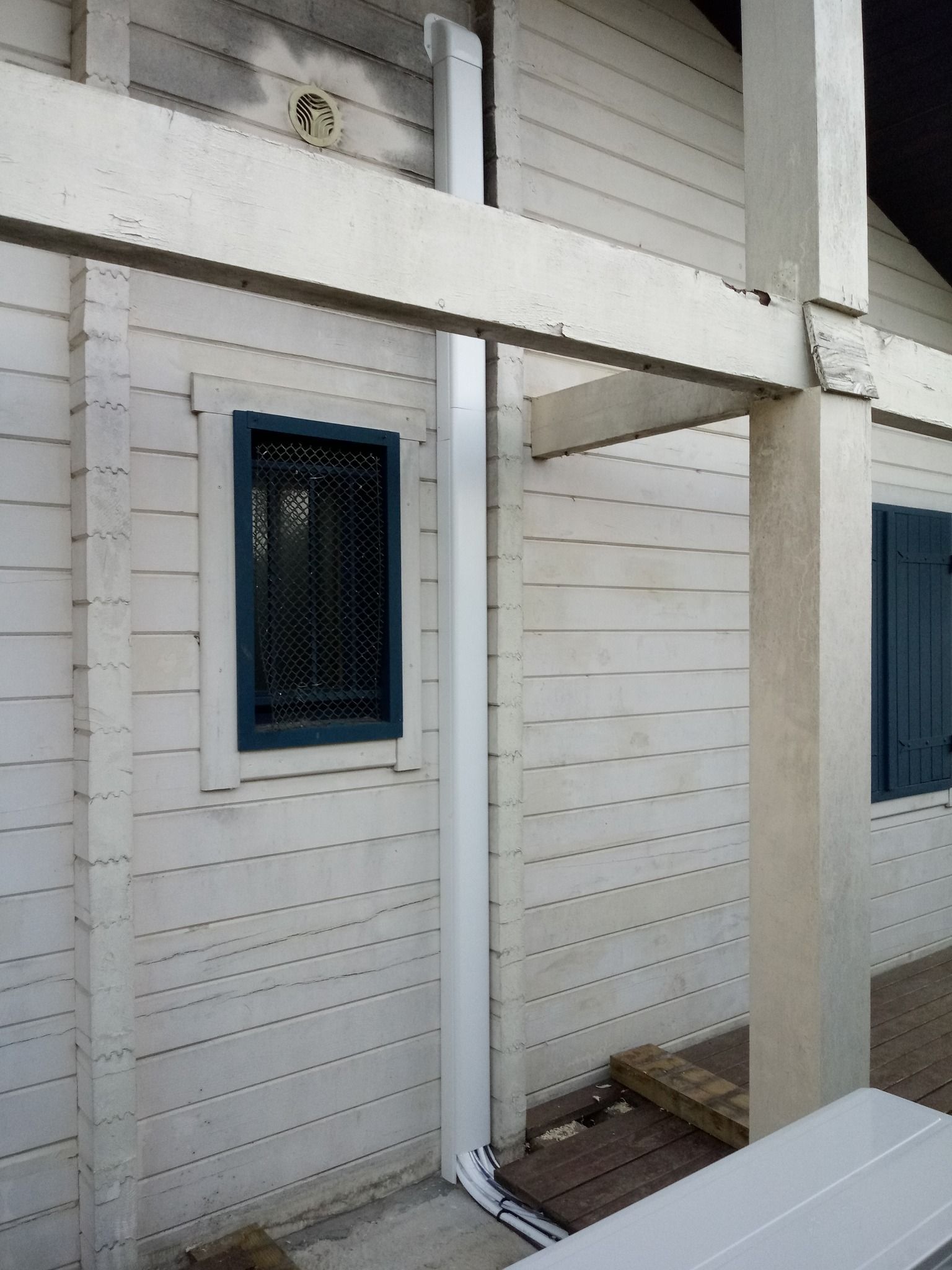 Bâtiment blanc avec une fenêtre, des volets sombres et une gouttière blanche verticale.
