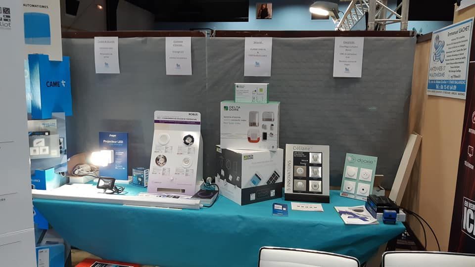 Table d'exposition commerciale avec échantillons de produits sur tissu bleu sarcelle, panneaux et fond blanc.