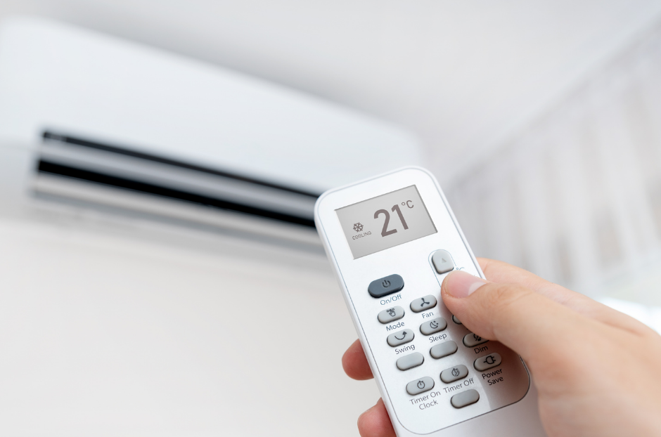 Main utilisant la télécommande du climatiseur, réglée à 21 degrés, dirigée vers l'unité murale blanche.