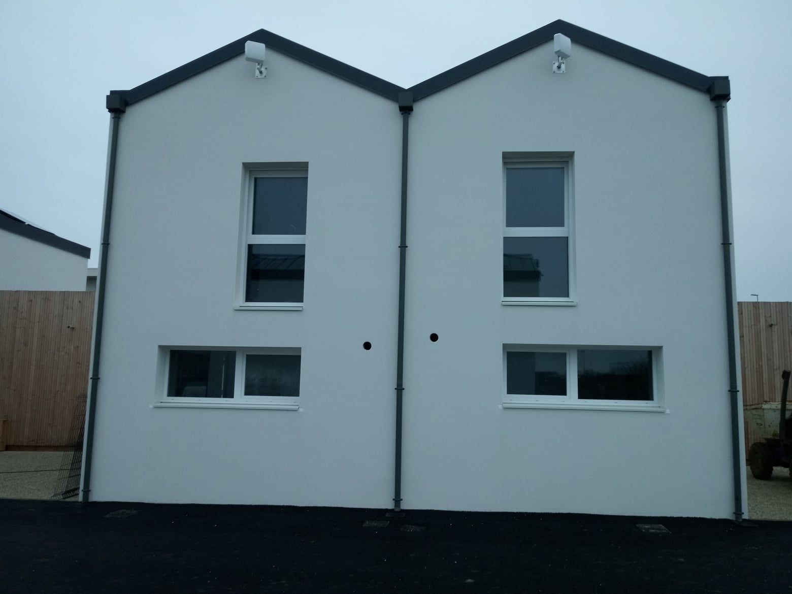 Deux bâtiments blancs reliés entre eux par des moulures sombres, chacun doté de deux fenêtres, par temps nuageux.