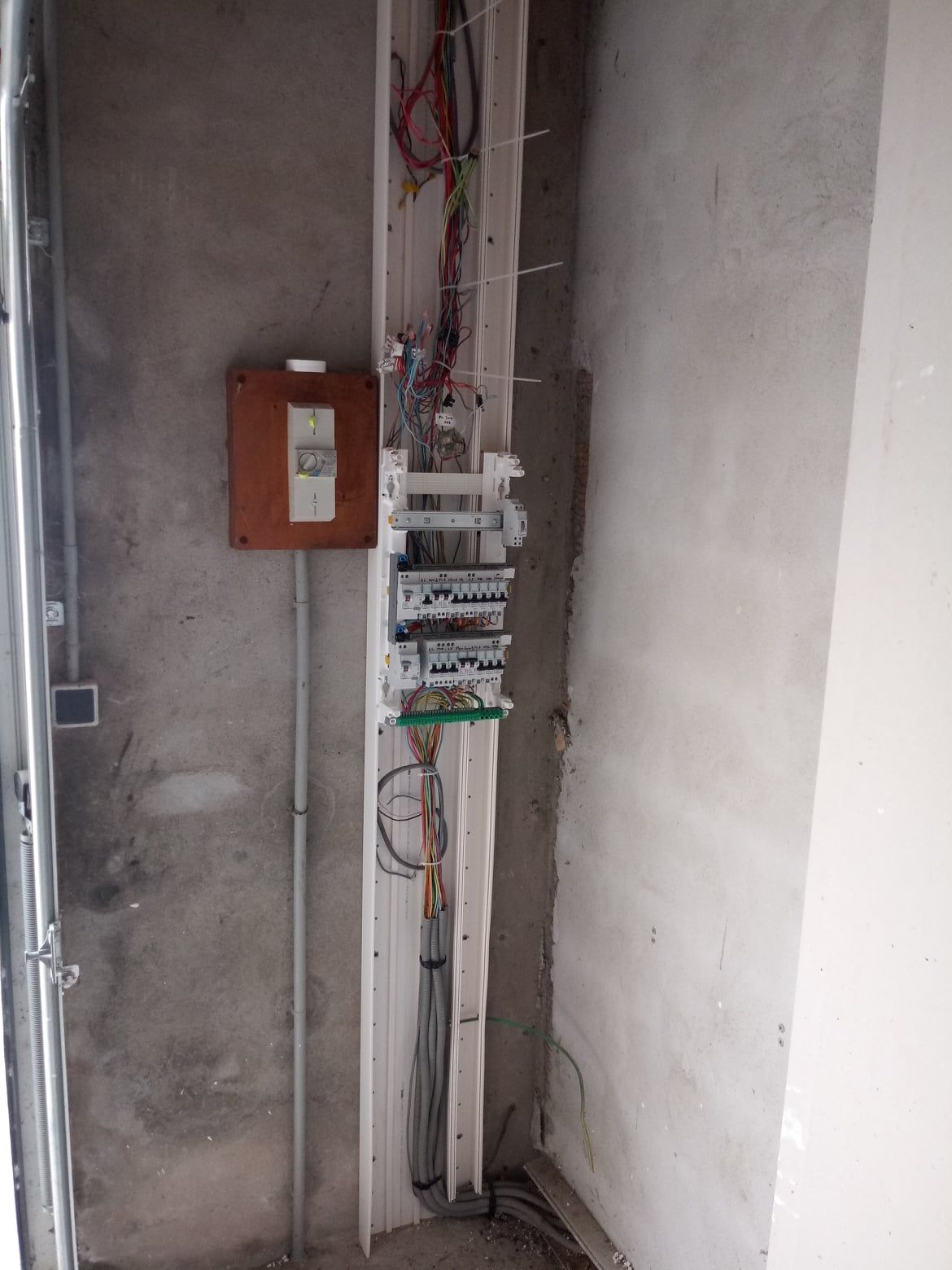 Panneau électrique et câblage installés dans un mur en béton. Les fils sont visibles, le panneau est marron.