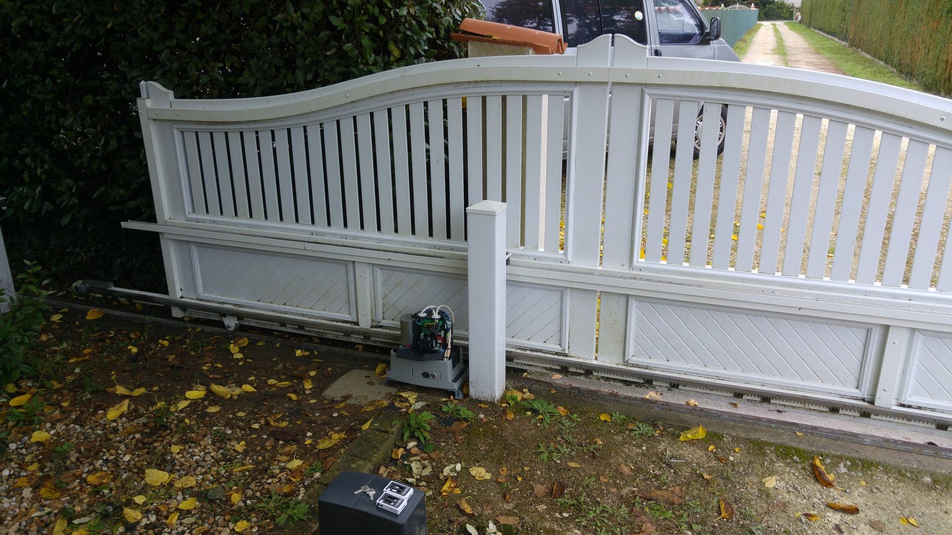 Portail coulissant automatique blanc partiellement ouvert sur une allée.