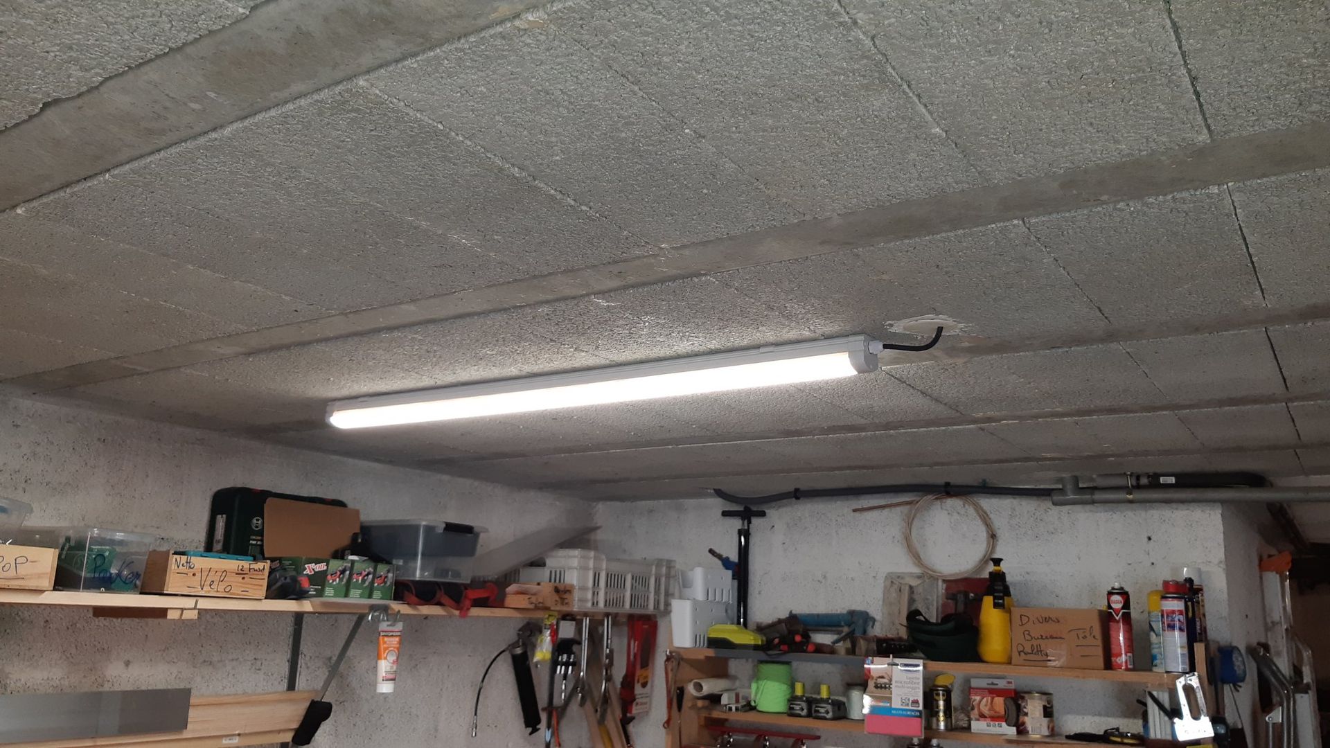 Un plafond de garage avec un éclairage fluorescent puissant. Des étagères remplies d'outils et de fournitures se trouvent en dessous.