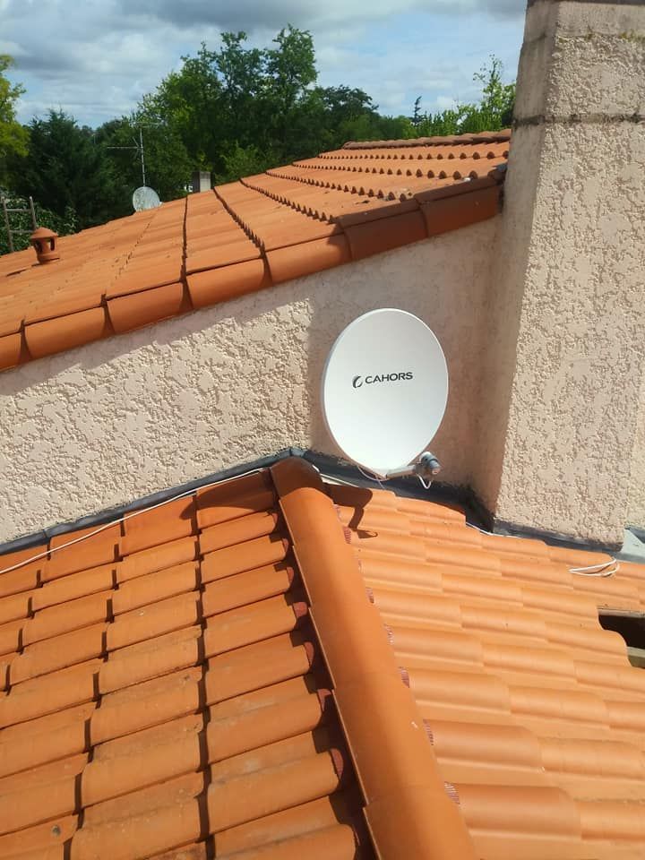 Antenne parabolique blanche montée sur un mur en stuc au-dessus d'un toit en tuiles d'argile.