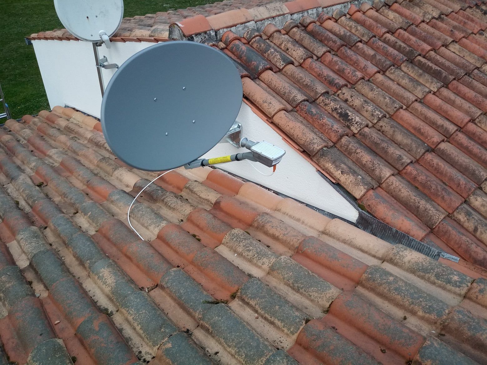 Antenne parabolique sur un toit de tuiles rouges.