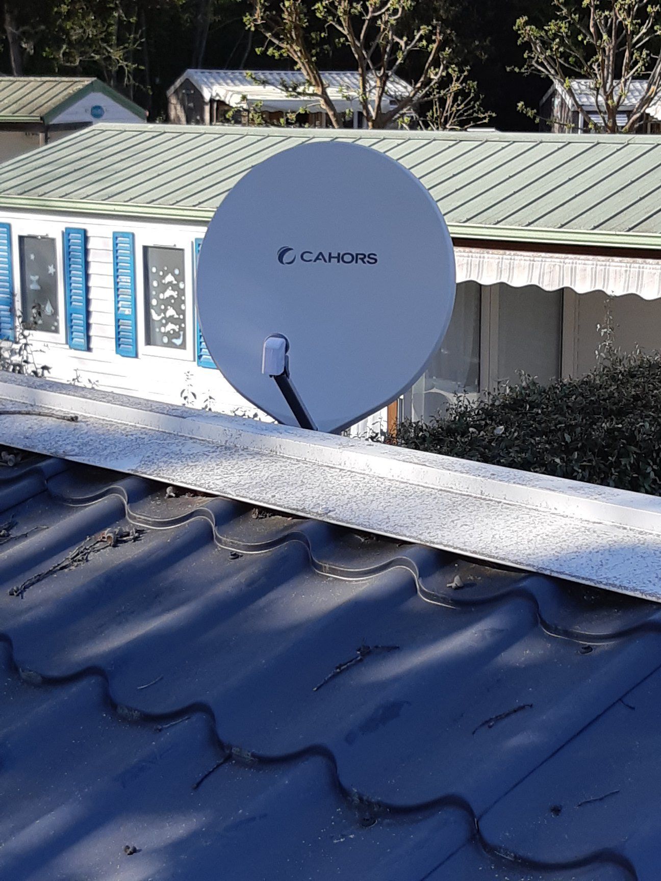 Une antenne parabolique blanche montée sur un toit bleu devant un bâtiment blanc.