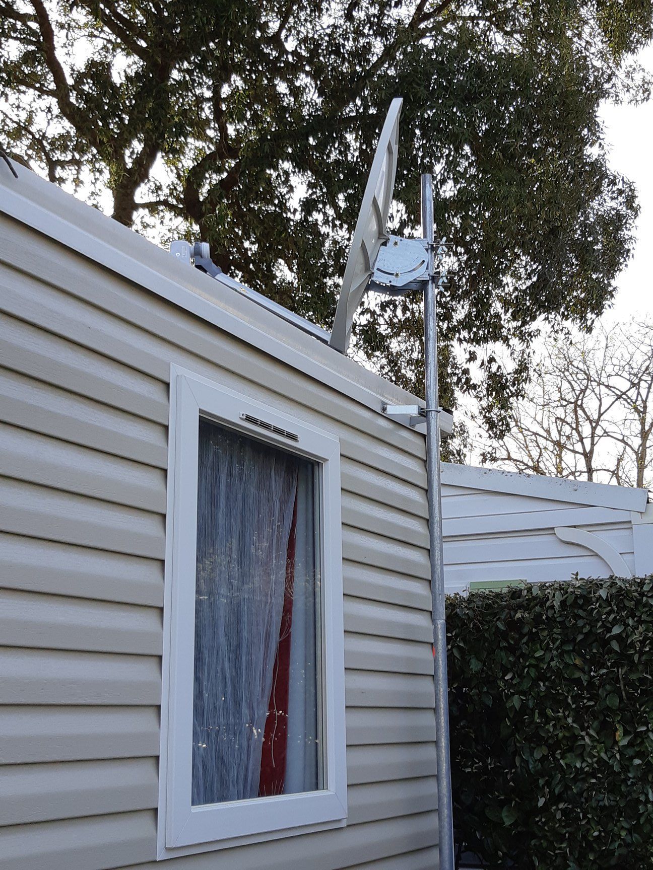 Une antenne parabolique montée sur un poteau métallique à côté d'un mobil-home blanc.