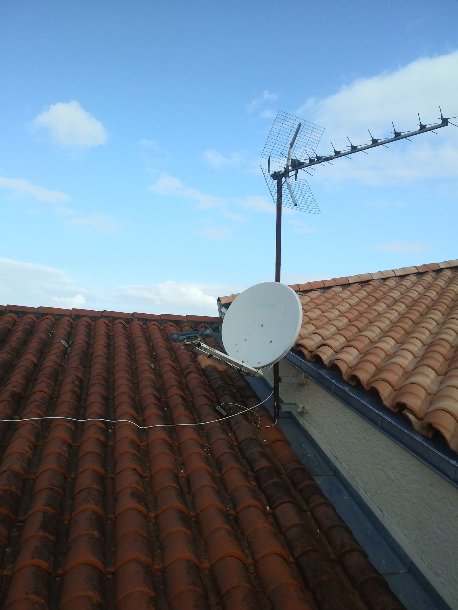 Antenne de télévision et parabole sur un toit de tuiles rouges contre un ciel bleu.
