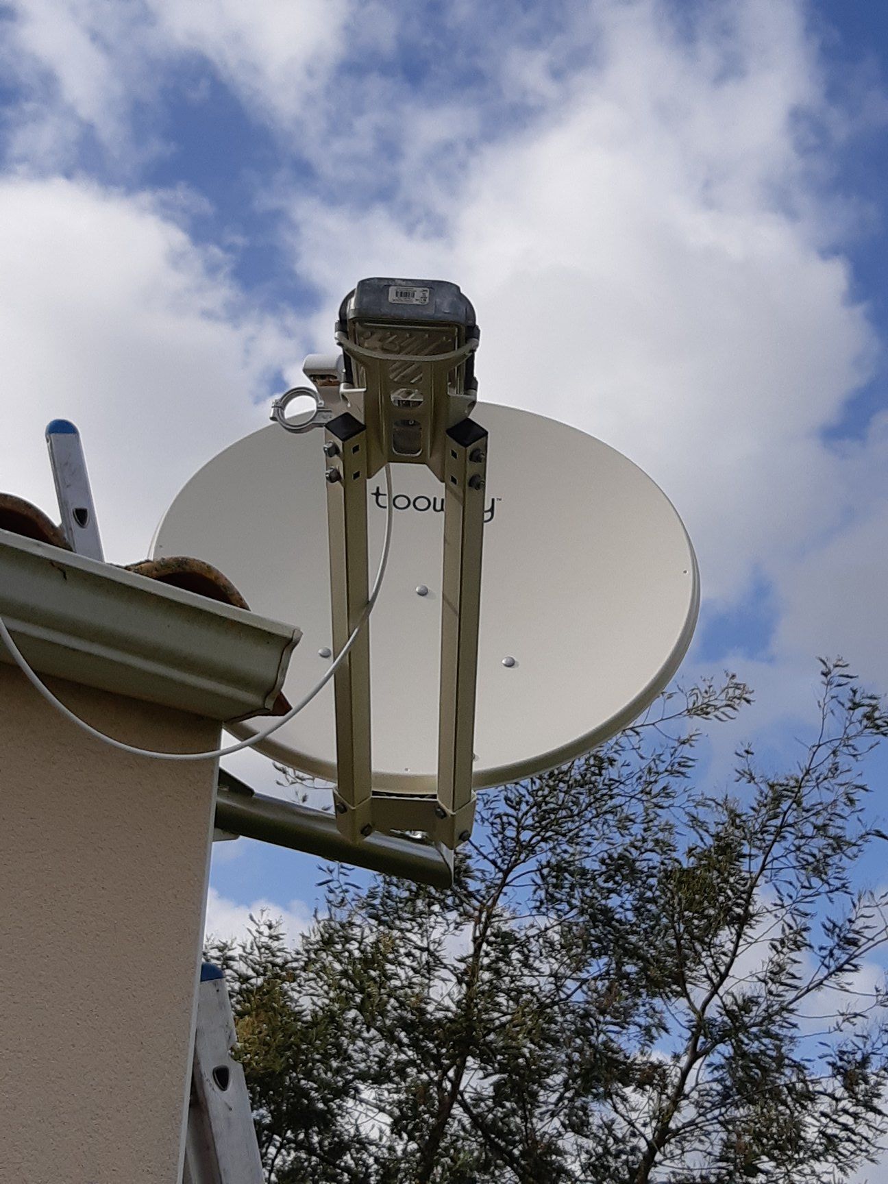 Une antenne parabolique blanche montée sur le côté d'une maison contre un ciel nuageux.