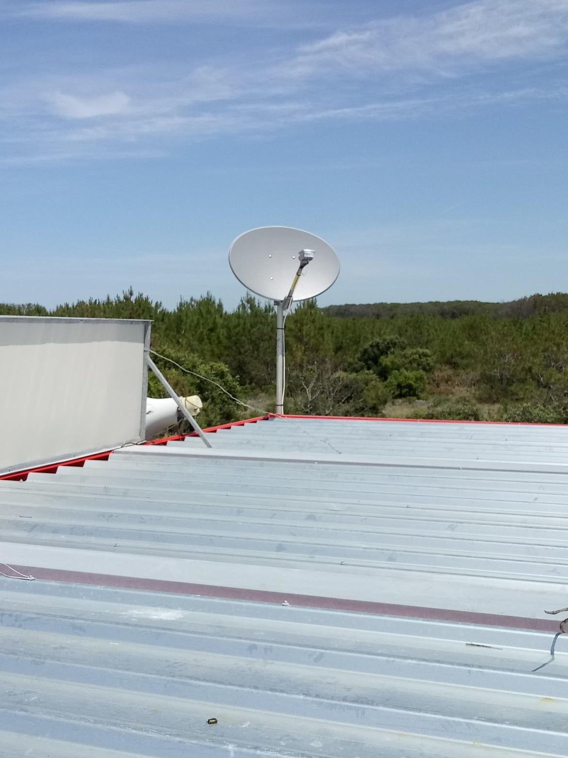Une antenne parabolique montée sur un toit en tôle ondulée sous un ciel bleu vif.