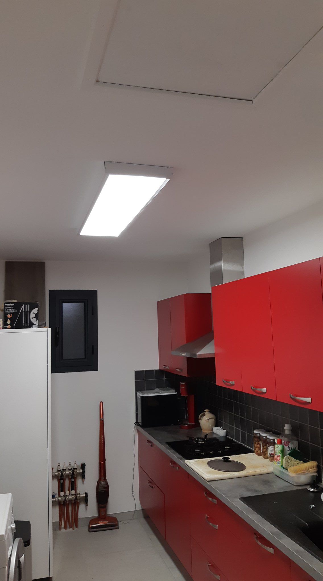 Cuisine avec armoires rouges, électroménagers en acier inoxydable et un plafonnier rectangulaire lumineux.