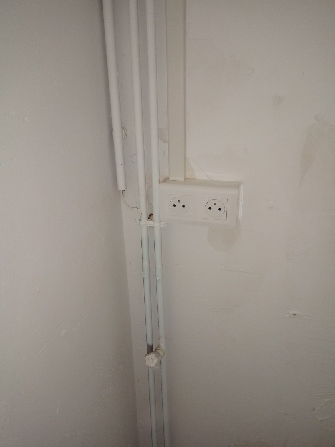 Mur blanc avec prise électrique et tuyaux.
