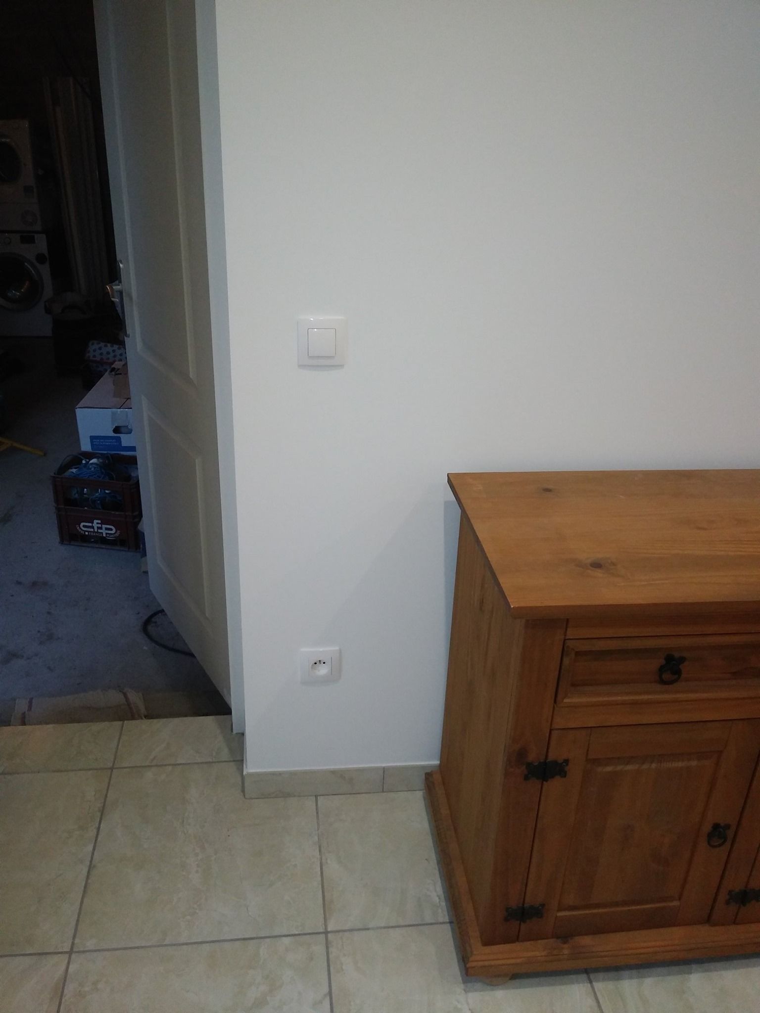 Mur blanc avec interrupteur et prise de courant près de l'armoire en bois et de la porte.