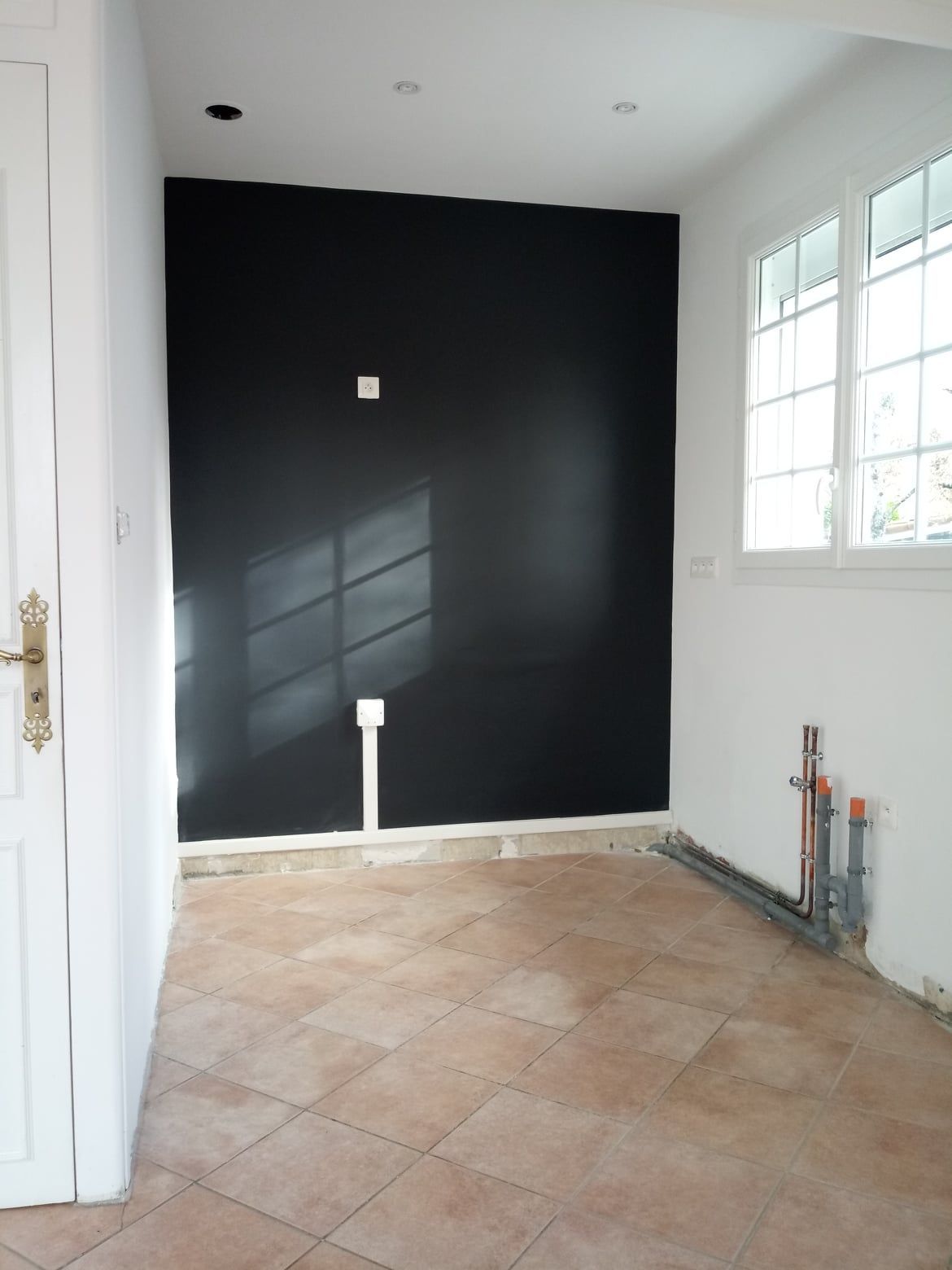 Une pièce avec un mur d'accent noir, des murs blancs, un sol carrelé et une fenêtre.