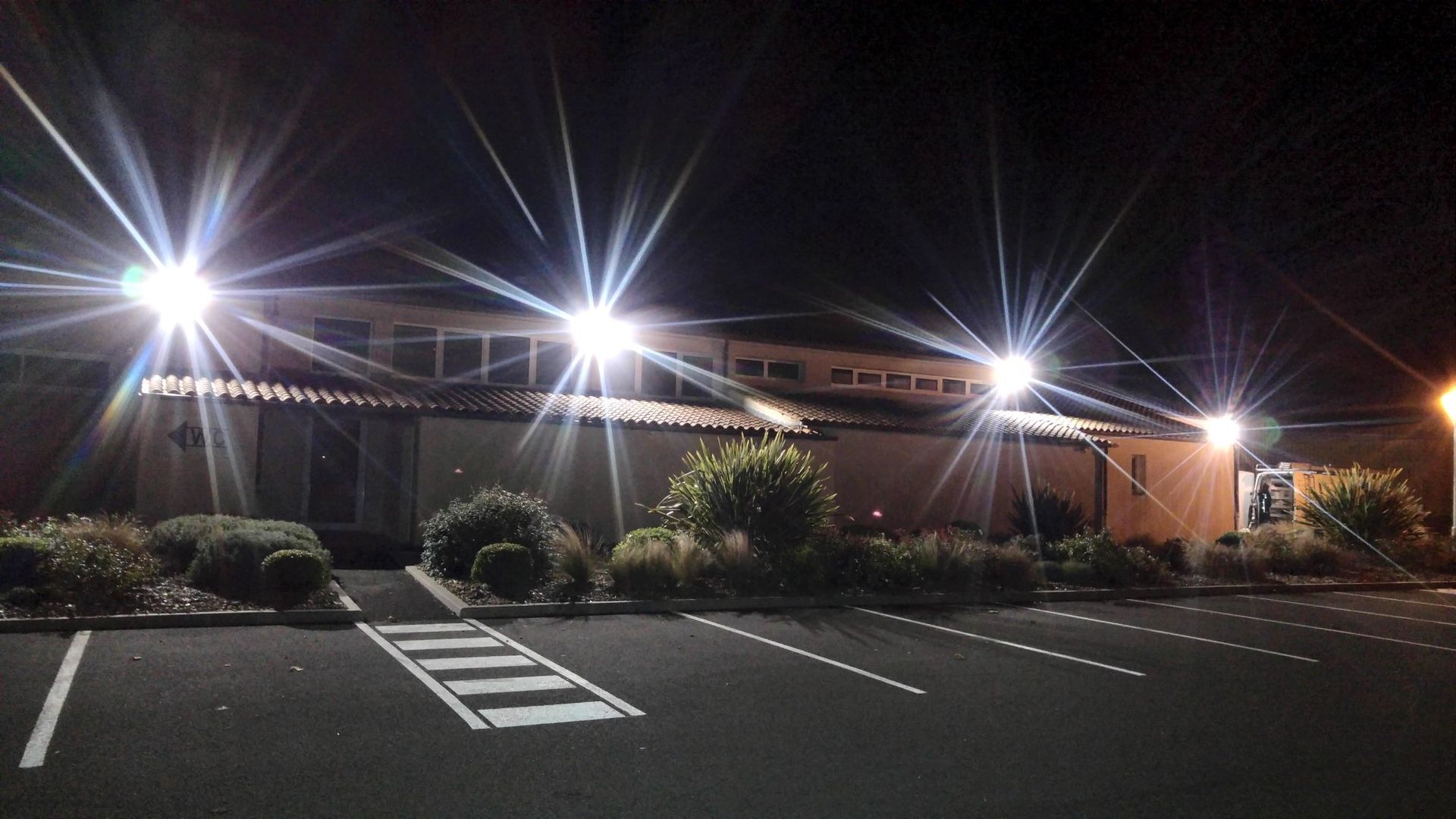 Un bâtiment la nuit avec des lumières vives illuminant la façade et un parking.