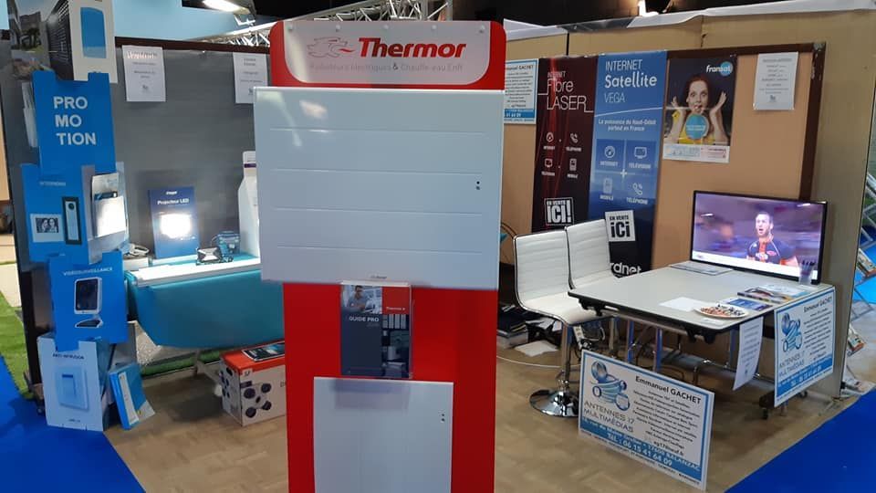 Un stand Thermor lors d'un salon professionnel présente un radiateur blanc sur un support rouge, avec des panneaux promotionnels et un petit téléviseur.