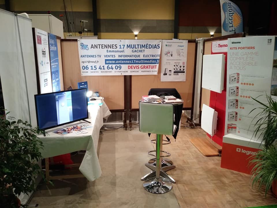 Stand d'exposition avec TV, tabourets de bar et matériel promotionnel ; panneau visible.