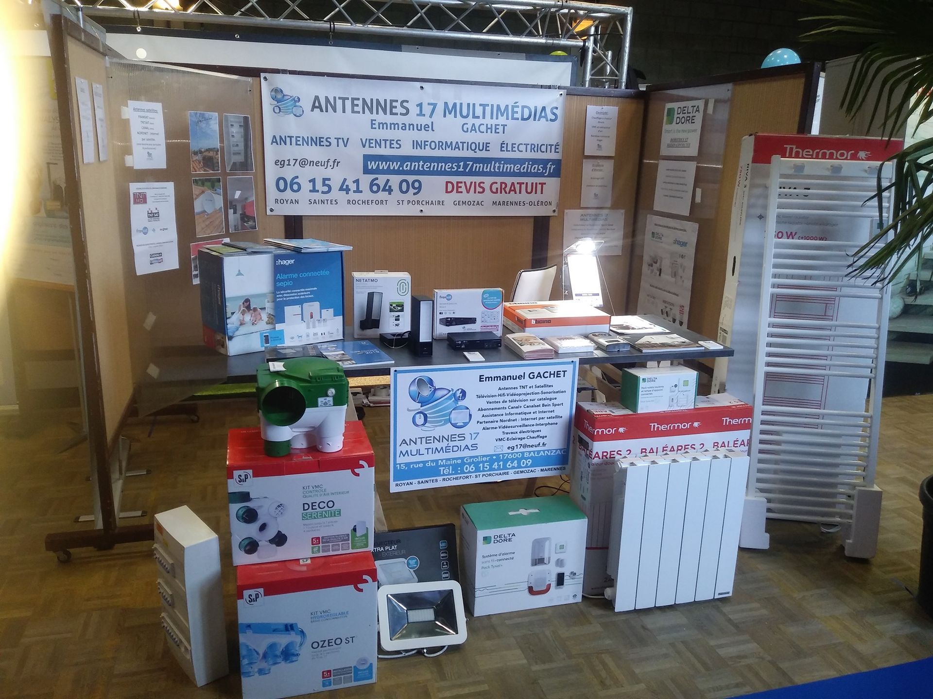 Un stand d'exposition présente des produits électroniques, avec une enseigne et diverses boîtes de produits et brochures.