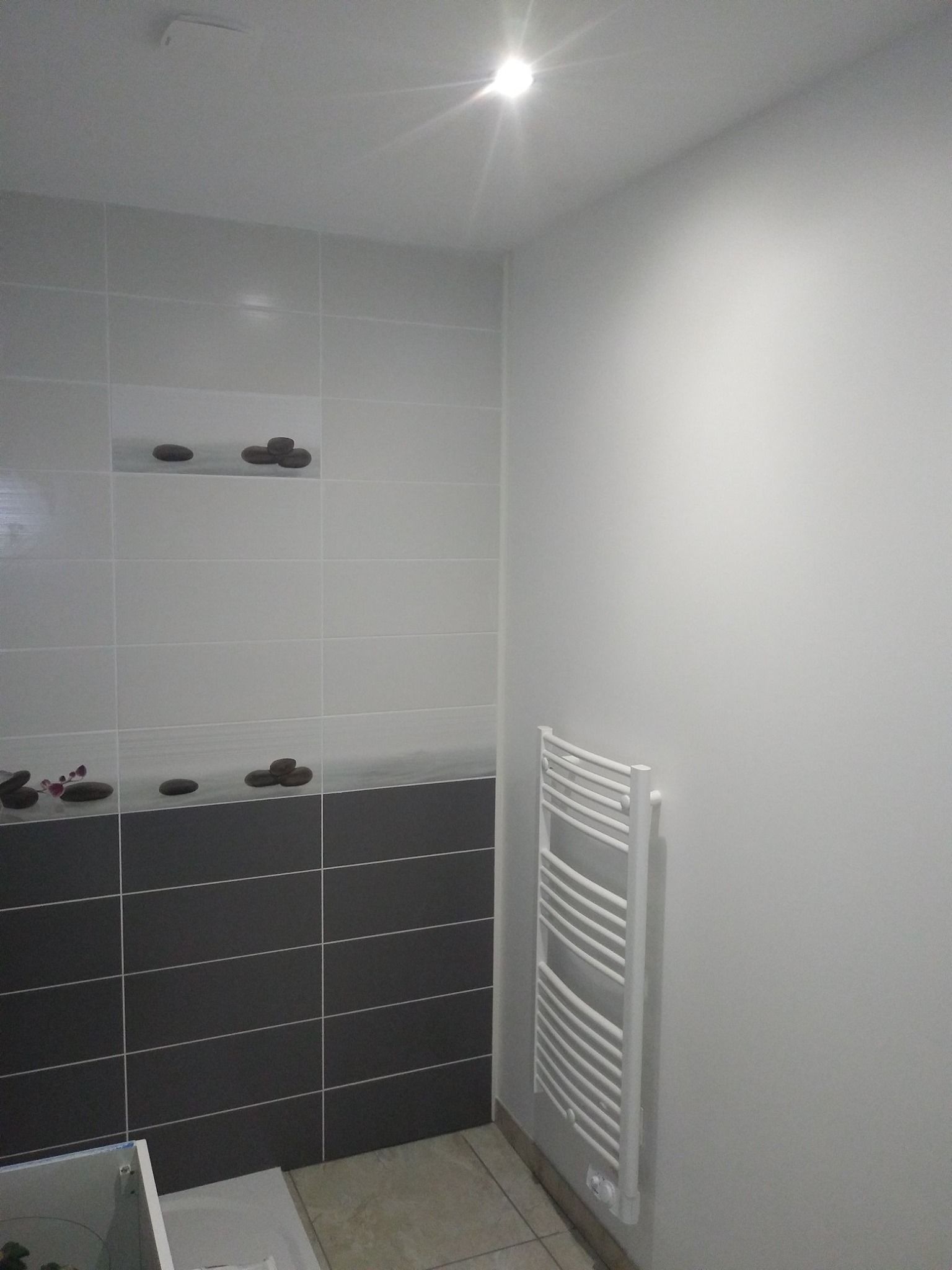 Salle de bains avec sèche-serviettes blanc, murs et carrelage gris et meuble bas gris foncé.