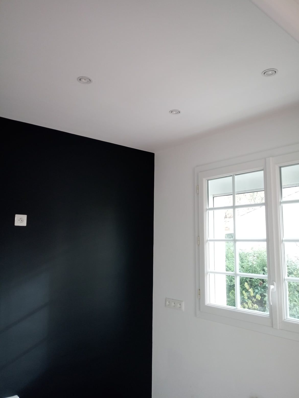 Mur d'accent noir, fenêtre blanche avec grille et plafonniers.