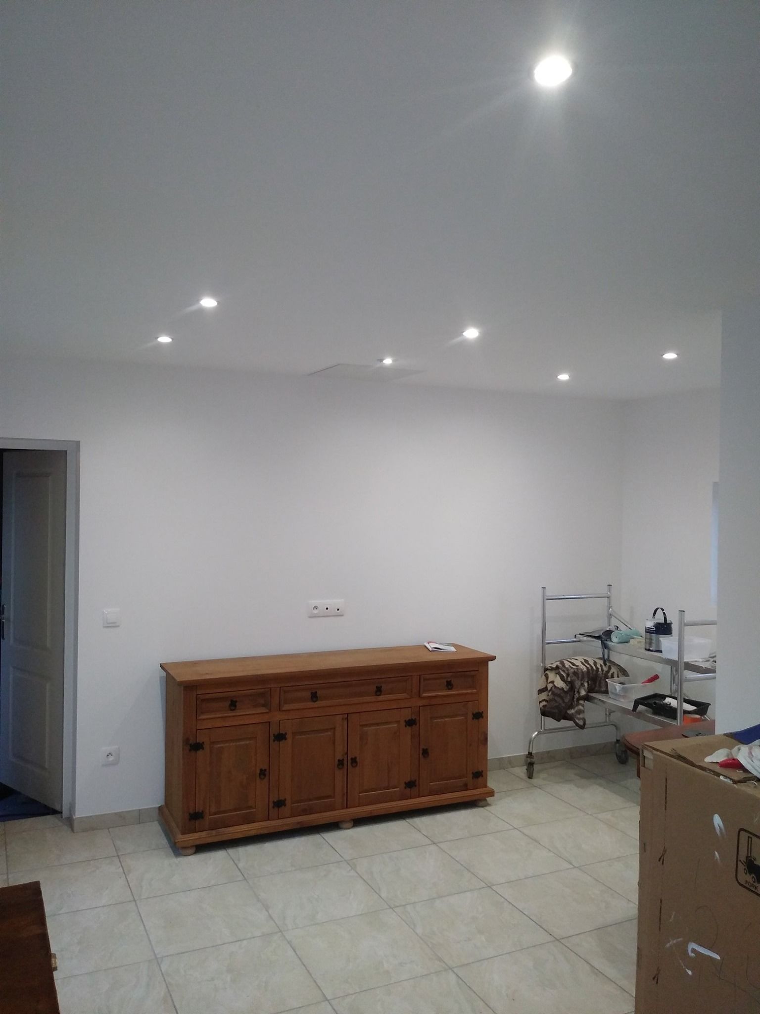 Armoire en bois contre un mur blanc, éclairage encastré, sol carrelé.