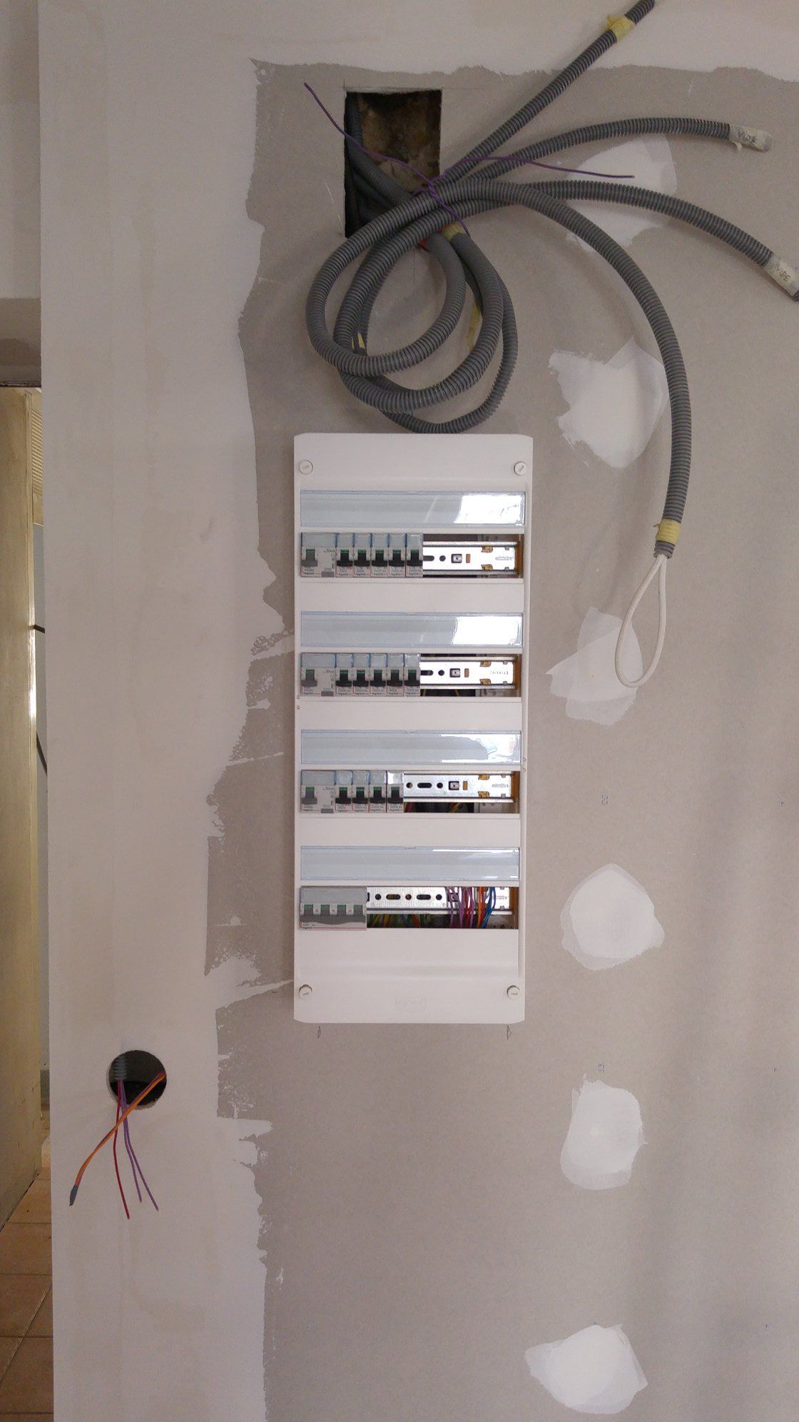Panneau électrique installé sur un mur partiellement plâtré avec câblage exposé.