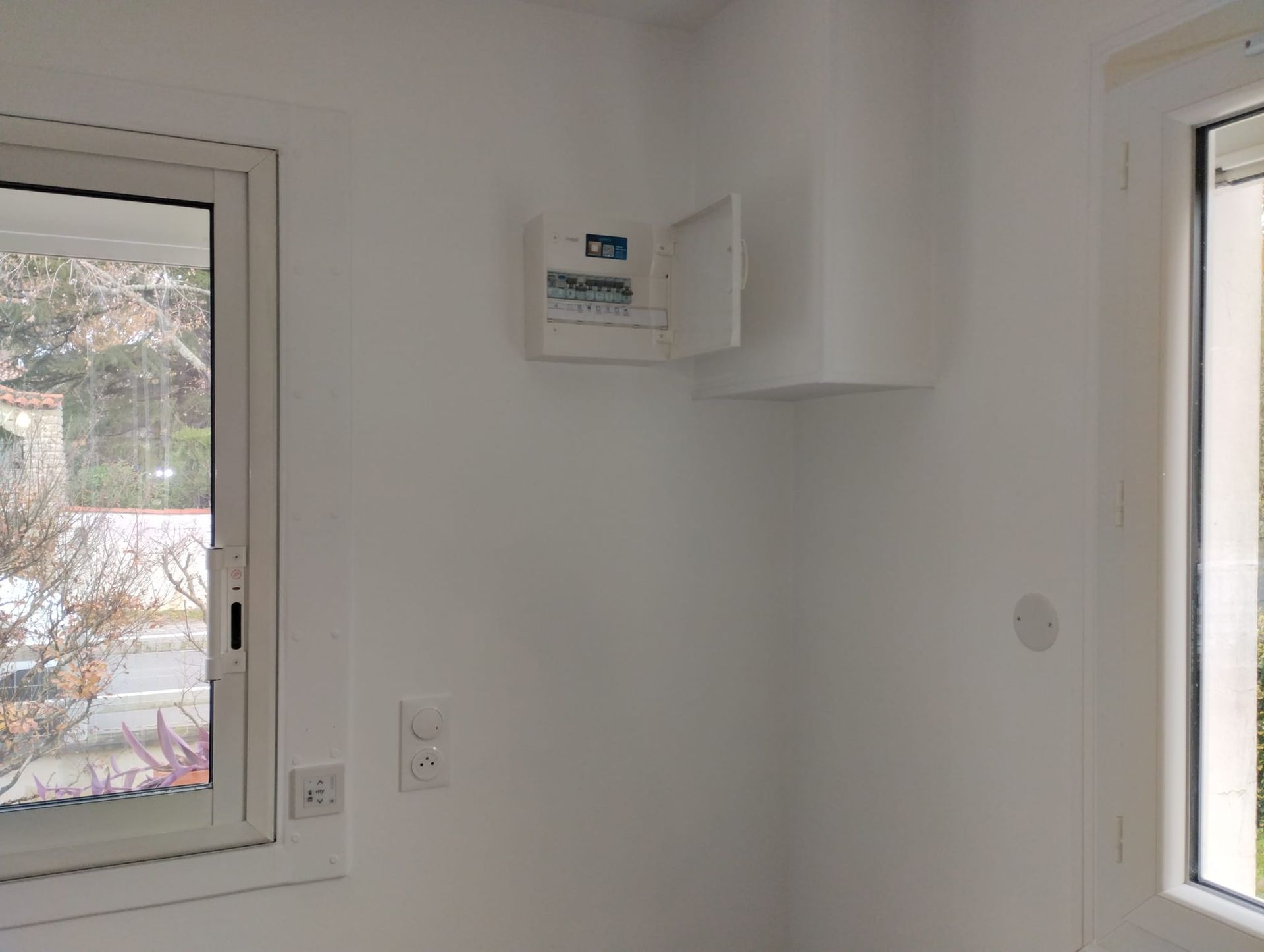 Intérieur blanc avec panneau électrique, fenêtre et interrupteur sur un mur blanc.