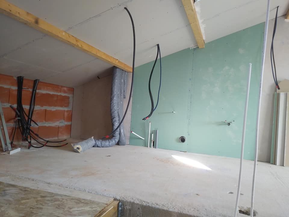 Chantier de construction intérieur avec mur de briques apparentes, cloisons sèches et fils ; espace inachevé et lumineux.