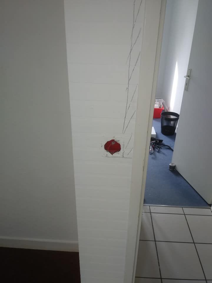 Un mur blanc avec une tache rouge et une porte donnant sur un couloir.