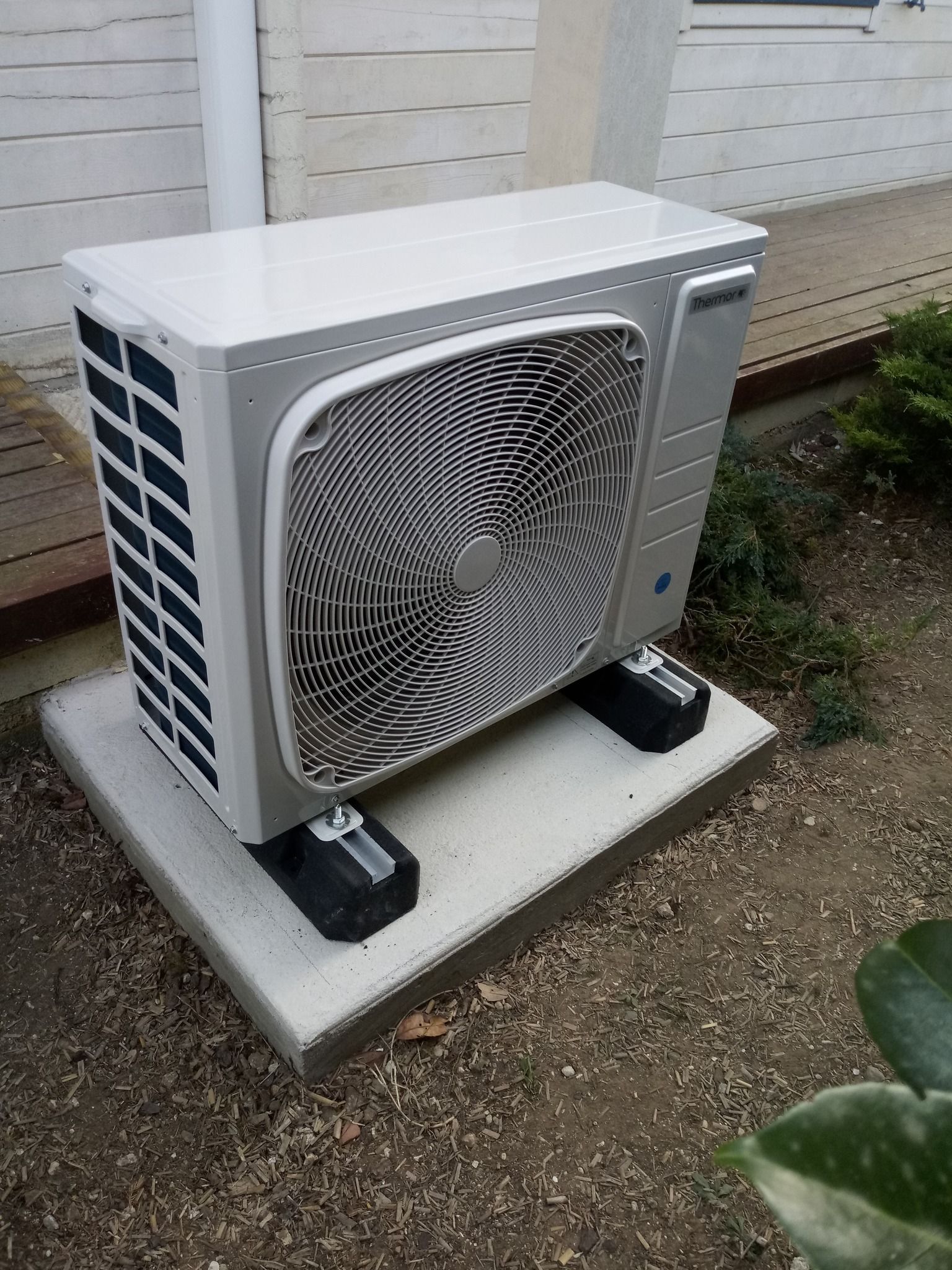 Unité de climatisation sur une dalle de béton à l'extérieur; couleurs gris et blanc.