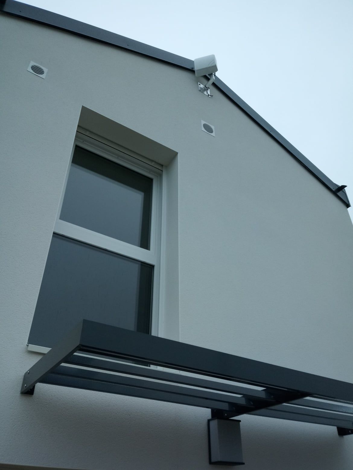 Extérieur d'un bâtiment blanc avec une fenêtre, un auvent et une caméra de sécurité.