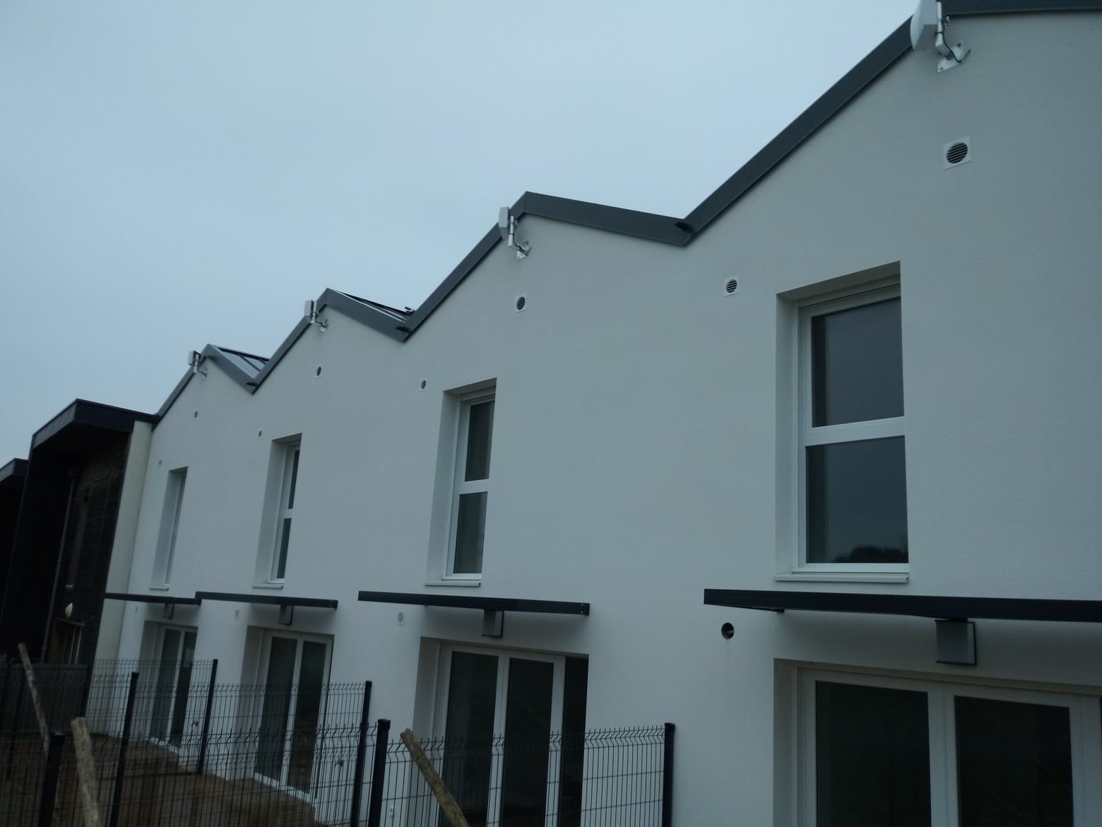 Rangée de maisons de ville blanches avec des lignes de toit, des fenêtres et des auvents noirs.