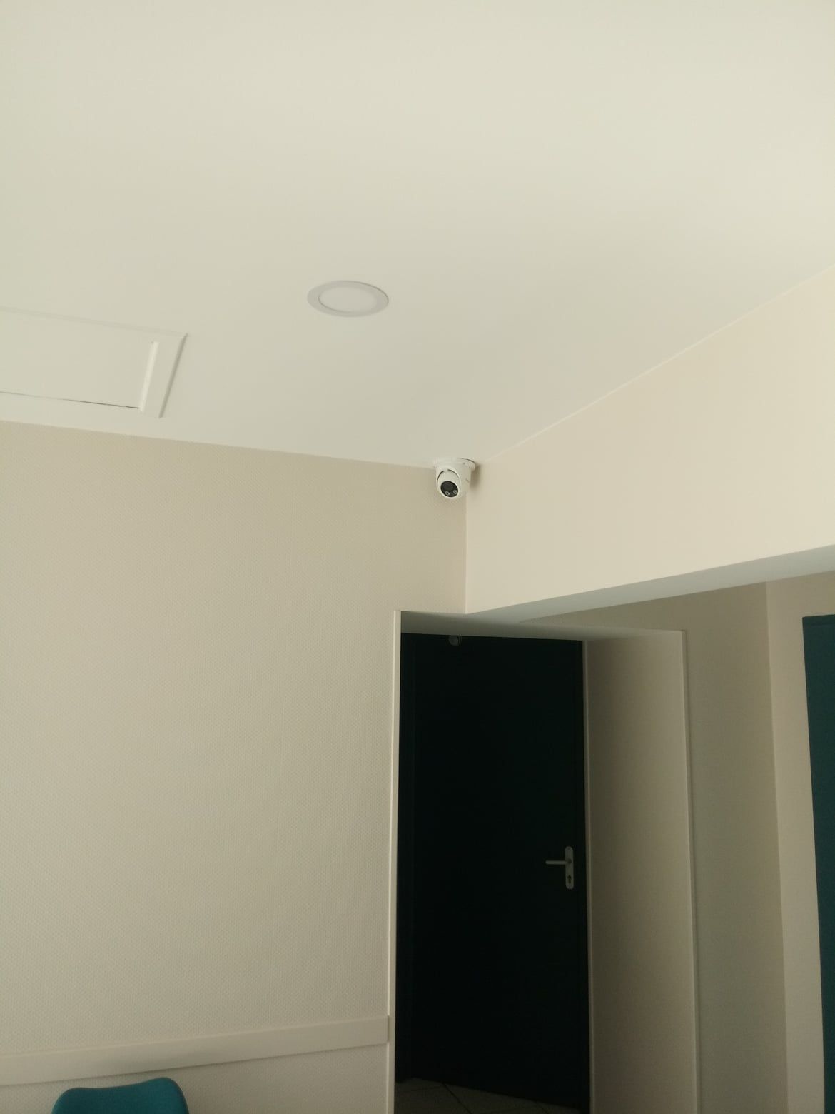 Caméra de sécurité installée dans le coin d'une pièce, donnant sur une porte sombre et des murs crème.