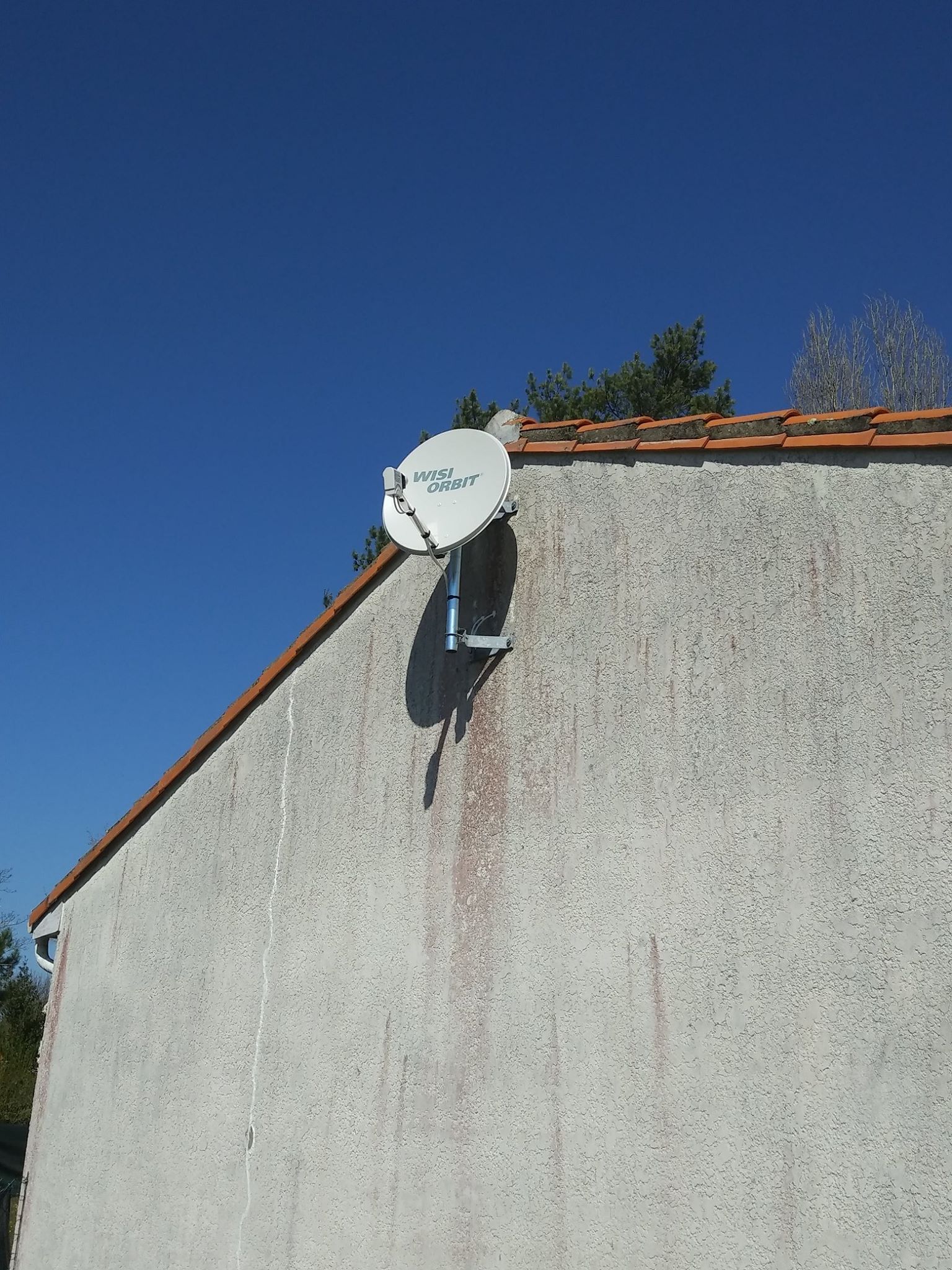 Antenne parabolique montée sur le côté texturé et clair d'un bâtiment sous un ciel bleu clair.