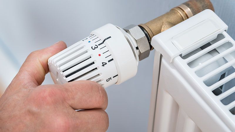 Eine Person stellt einen Thermostat an einem Heizkörper ein