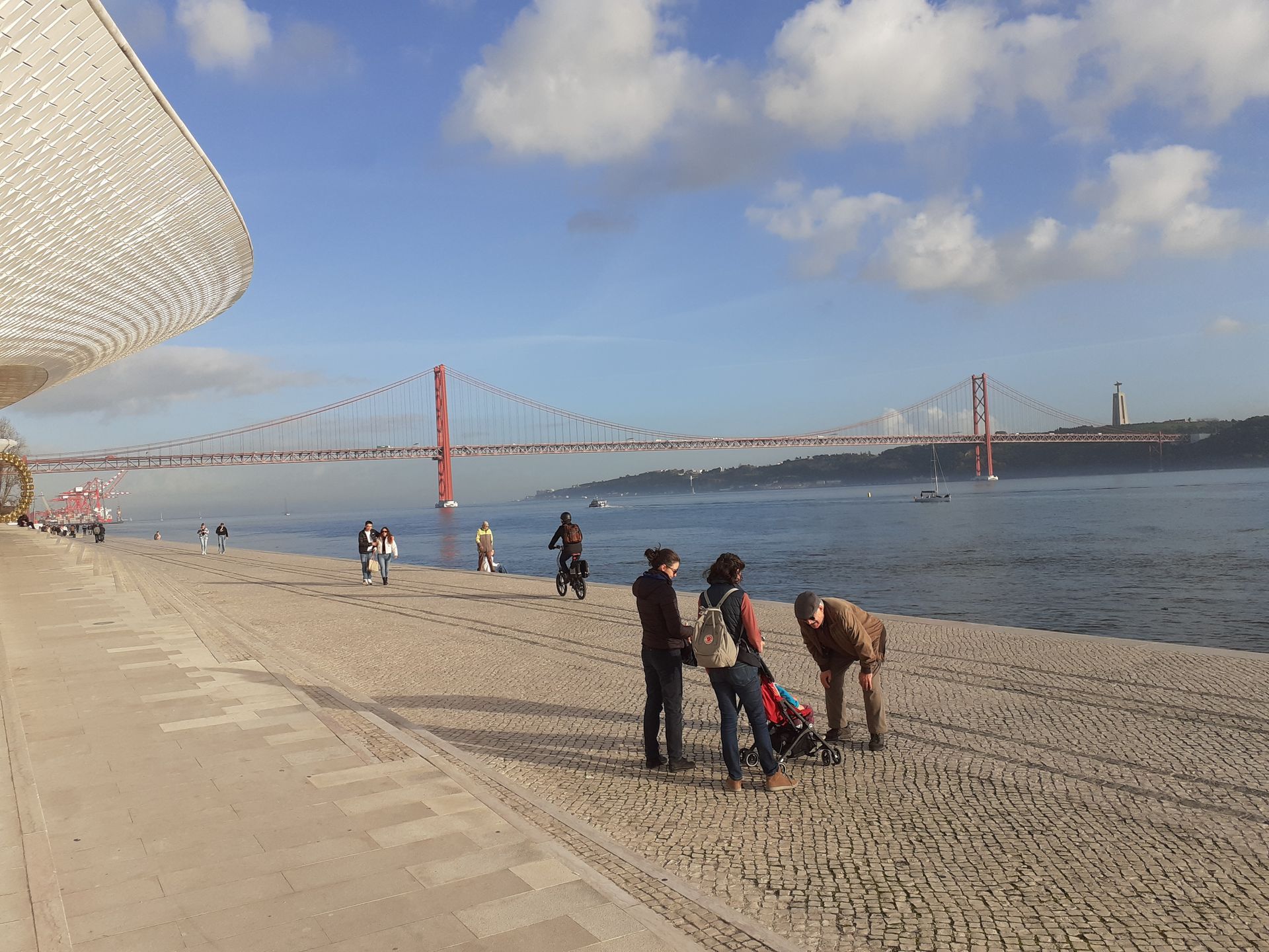 Rive d'un fleuve avec promeneurs et pont métallique en arrière plan