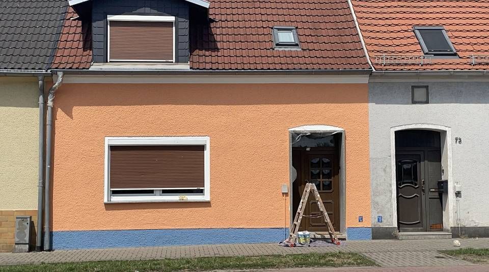 Eine Leiter steht vor einem Haus, das in orange gestrichen wird.