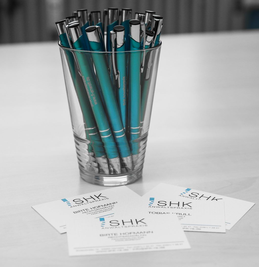 Ein Glas mit blauen Stiften steht auf einem Tisch neben Visitenkarten