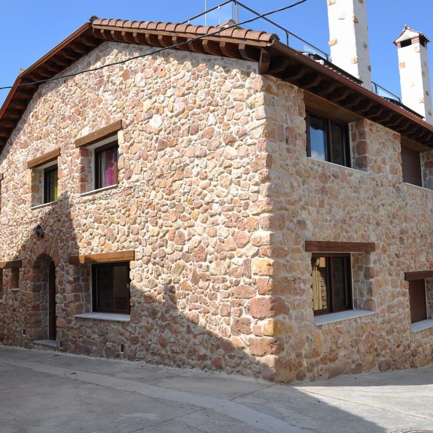 Casa de piedra con molduras y ventanas marrones, techo de tejas rojas, en una calle adoquinada.