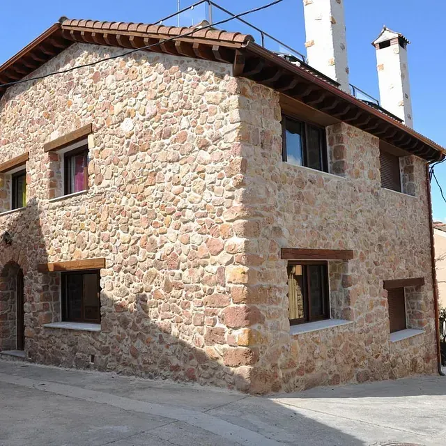 Casa de piedra con molduras, ventanas y tejas de color marrón, en entorno de calle.
