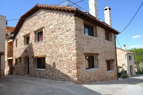 Casa de piedra con techo marrón y molduras de ventanas en una calle adoquinada.
