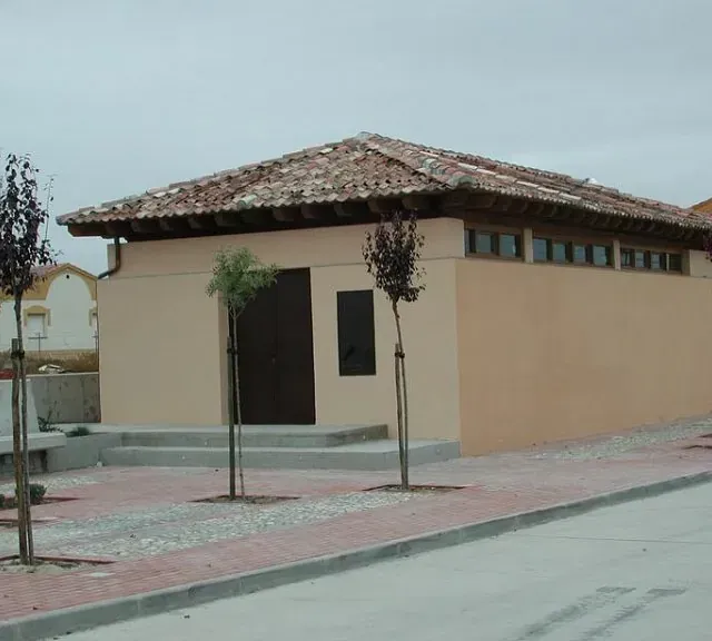 Edificio de color tostado con techo de tejas marrones, puerta y ventanas pequeñas.