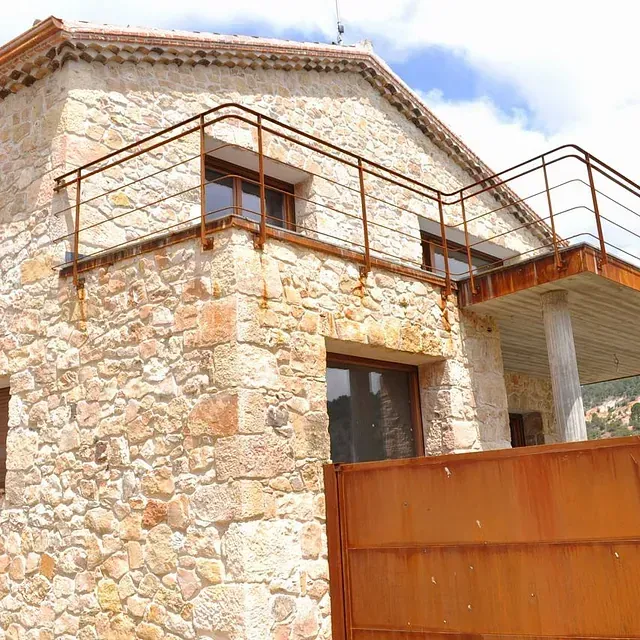 Casa de piedra con reja y puerta de metal oxidado.