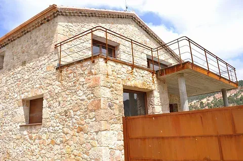 Casa de piedra con balcón y portón de metal oxidado. Edificio marrón y canela, con cielo azul de fondo.