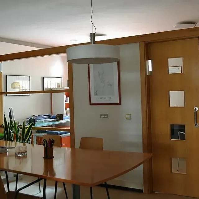 Sala de conferencias con mesa de madera, sillas y obras de arte enmarcadas. A la derecha hay una puerta con pequeñas ventanas cuadradas.