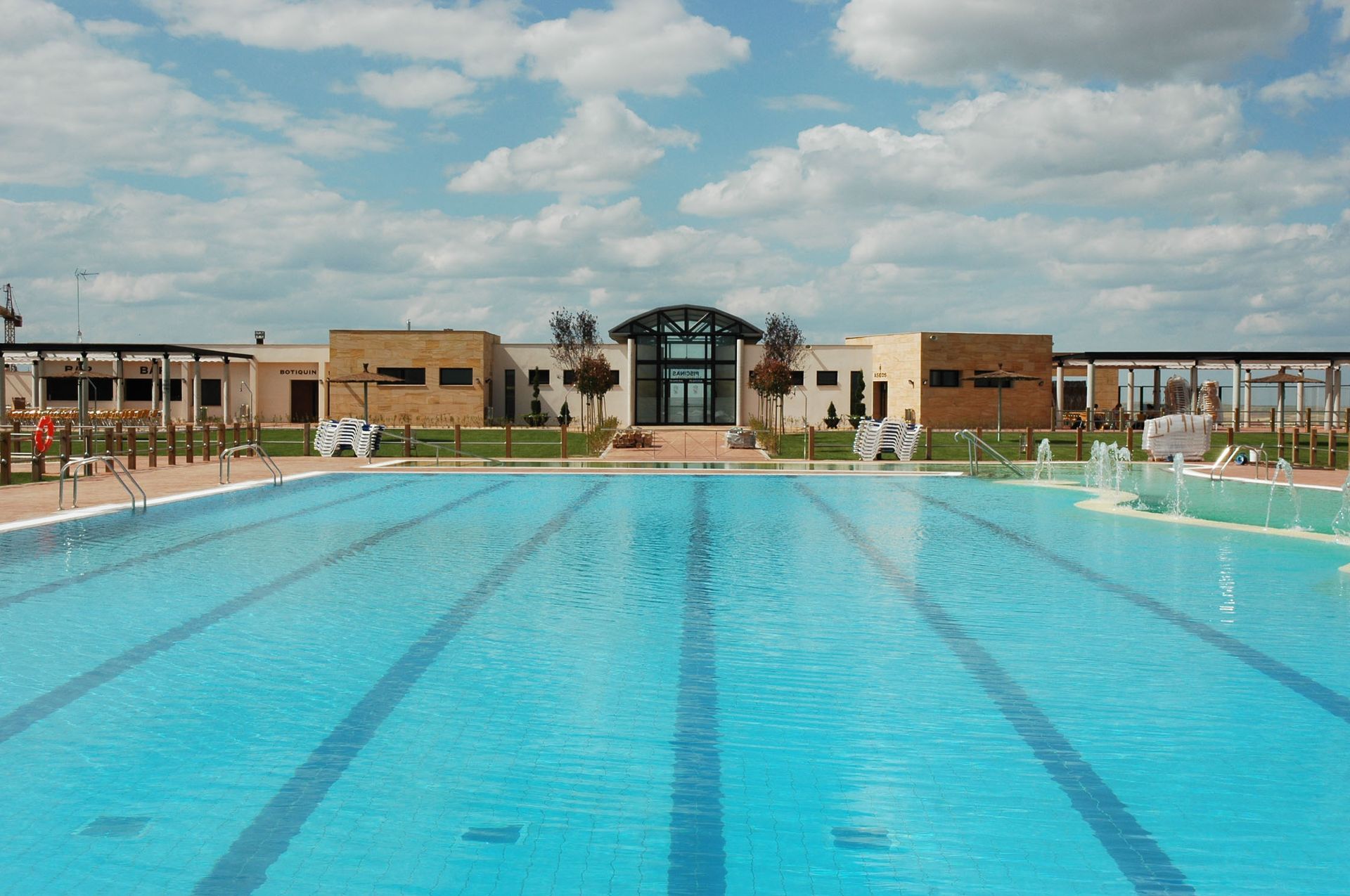 Piscina frente a un edificio de color canela con un cielo azul y algunas nubes.
