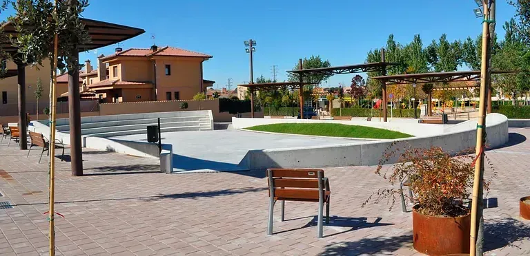 Un anfiteatro al aire libre con árboles y edificios al fondo. Cielo despejado.
