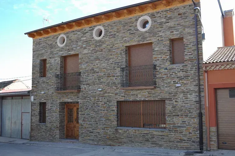 Edificio de piedra de dos pisos con molduras de madera, persianas y balcones.