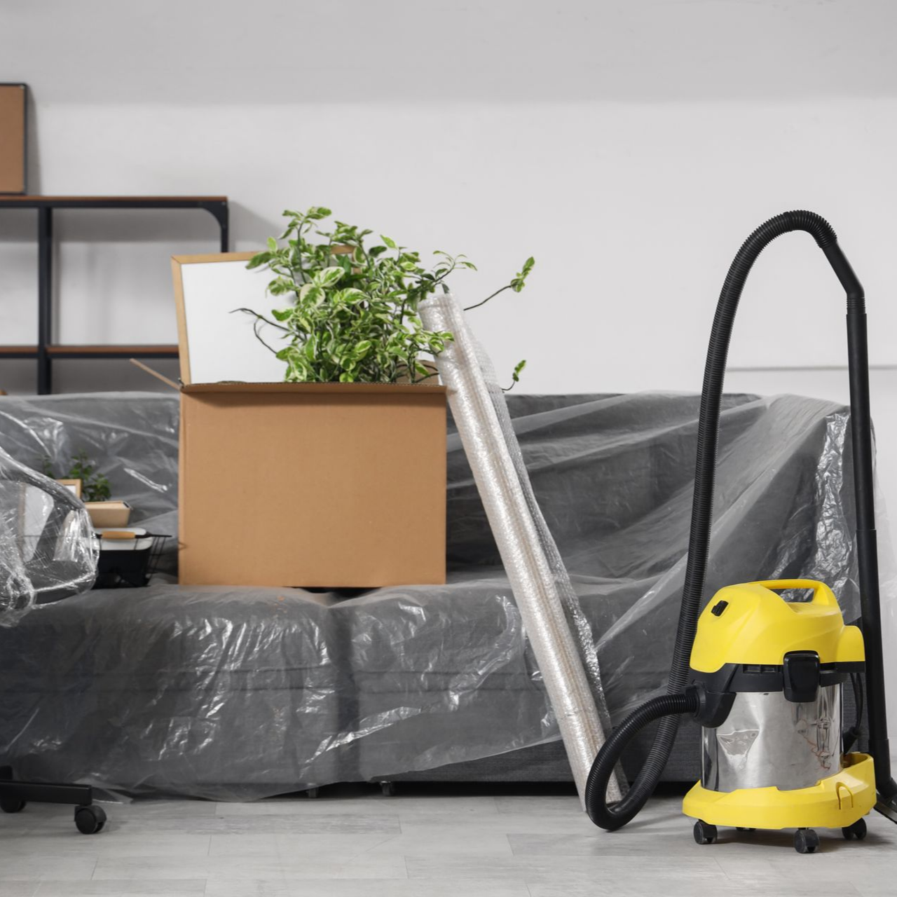 Une pièce avec des cartons de déménagement, un aspirateur et un canapé couvert.